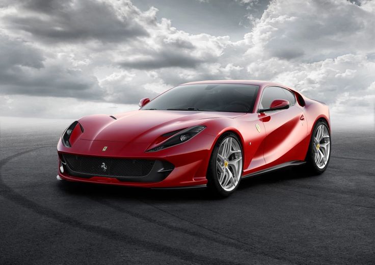 Sleek red sports car on asphalt under dynamic cloudy sky, showcasing modern design and aerodynamics.