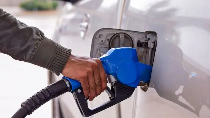 Person refueling a silver car at a gas station with a blue pump handle.