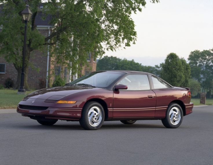 Saturn SC2 1993-95 - Engine Stories Red sports coupe parked on a residential street, showcasing its sleek design and vintage style.