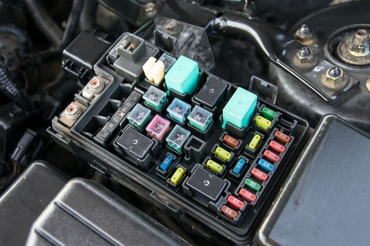 Signs Your Car Has a Blown Fuse _ YourMechanic Advice - Engine Stories Close-up of a car fuse box with various colored fuses and relays, showcasing detailed automotive components.