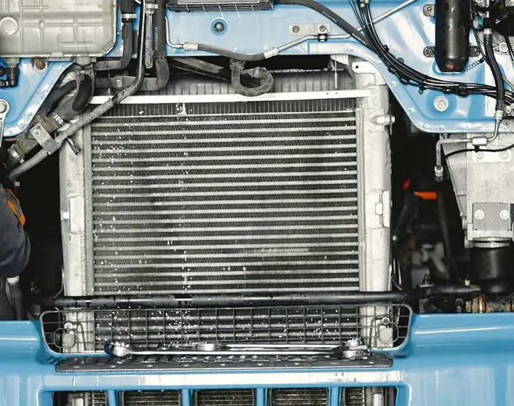 Close-up of a car radiator with visible engine components, showcasing automotive engineering details and mechanical design.