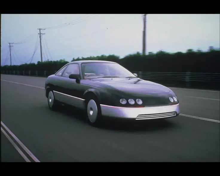 Toyota GTV 1987 - Engine Stories Sleek futuristic car driving on a highway, showcasing modern design and aerodynamic features in a dynamic motion shot.