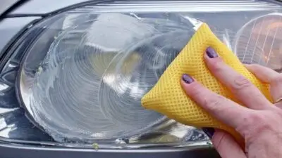 Cleaning a car headlight with a yellow sponge to restore clarity and enhance visibility.