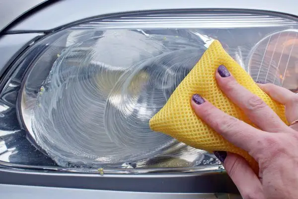 Cleaning a car headlight with a yellow sponge to restore clarity and enhance visibility.
