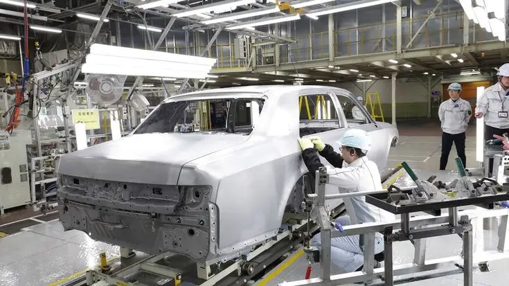 Workers assembling a car body in a modern automotive manufacturing plant.