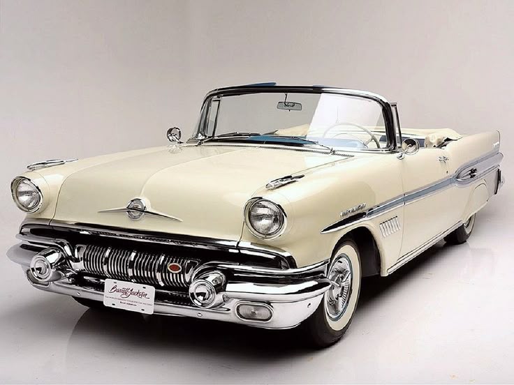 🚘Classic Cars Pontiac Bonneville 1957 - Engine Stories Classic ivory 1957 Pontiac convertible with chrome details on display in a studio, showcasing vintage design and luxury.