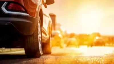 Red car on a sunny road during sunset, highlighting vibrant colors and travel vibe.