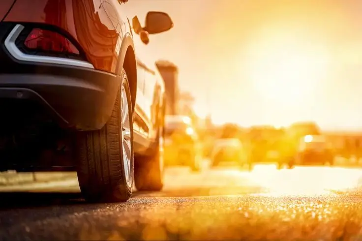 Red car on a sunny road during sunset, highlighting vibrant colors and travel vibe.