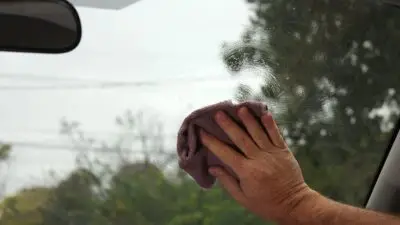 Hand cleaning a car windshield with a pink cloth. Clear glass for safer driving.