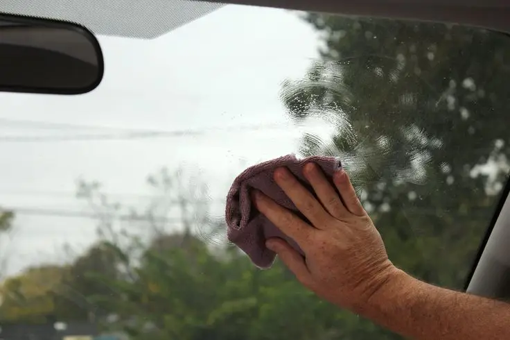Hand cleaning a car windshield with a pink cloth. Clear glass for safer driving.
