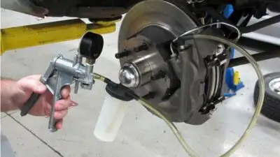 Mechanic using bleeder kit to flush brake fluid on car disc brakes in auto repair shop.