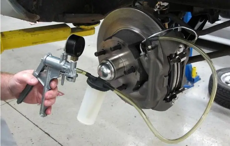 Mechanic using bleeder kit to flush brake fluid on car disc brakes in auto repair shop.