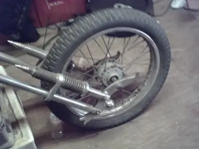 Close-up of a vintage motorcycle wheel, showcasing detailed spokes and suspension in a workshop setting.