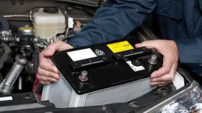 Mechanic installing a car battery under the hood, emphasizing automotive maintenance and repair services.