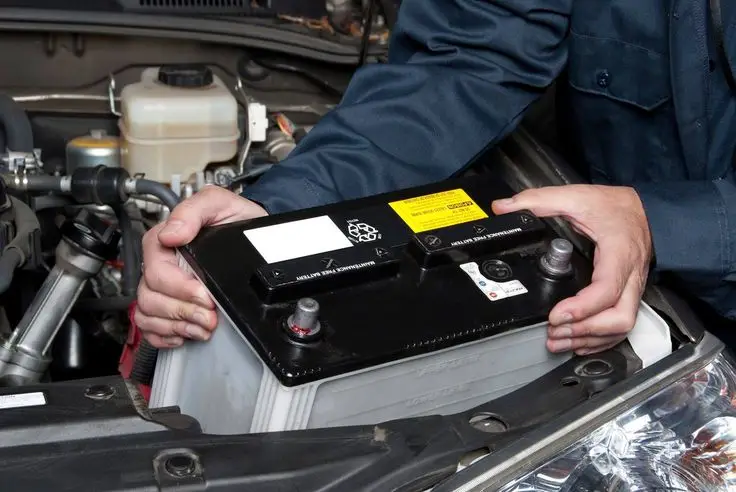Mechanic installing a car battery under the hood, emphasizing automotive maintenance and repair services.