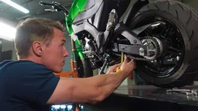 Mechanic fine-tuning the chain of a green motorcycle on a lift in a workshop.