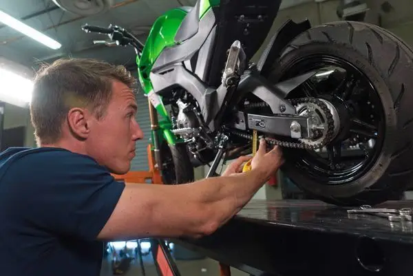 Mechanic fine-tuning the chain of a green motorcycle on a lift in a workshop.