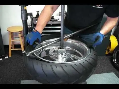 Technician changing a motorcycle tire using tools in a workshop setting, showcasing tire maintenance and repair.