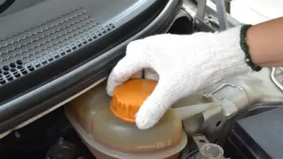 Gloved hand opening car radiator cap for maintenance, focusing on safety and vehicle care.