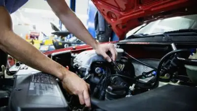 Mechanic working on a car engine in a workshop, focused on vehicle maintenance and repair.