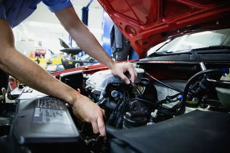 Mechanic working on a car engine in a workshop, focused on vehicle maintenance and repair.