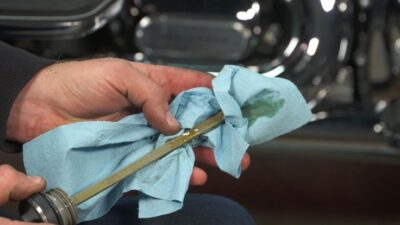 Person checking motorcycle oil dipstick with blue cloth, ensuring engine maintenance.