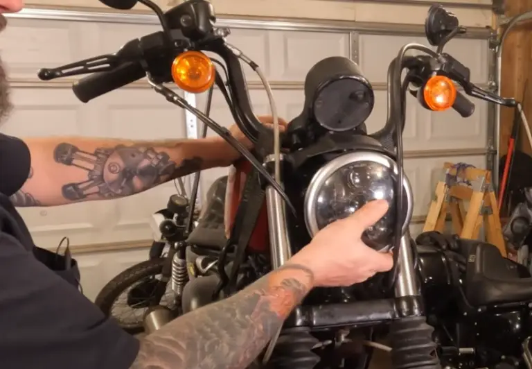 Mechanic adjusting motorcycle headlight in a garage; close-up of hands and bike parts.