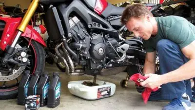 Man changing motorcycle oil with containers and tools nearby in garage.