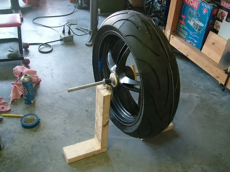 Motorcycle tire and wheel on DIY balancing stand in workshop, surrounded by tools and maintenance equipment.