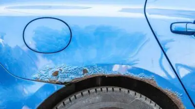Close-up of a blue car with rust damage above the rear tire, highlighting need for vehicle maintenance and corrosion prevention.