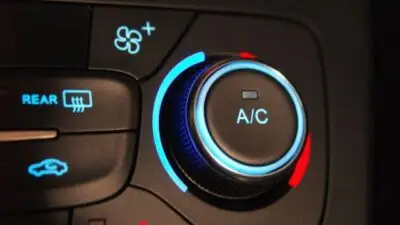 Close-up of a car air conditioning control panel with A/C button and temperature adjustment dial.