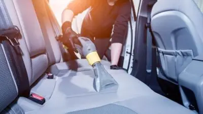 Person cleaning car seats with a vacuum extractor in the backseat area, emphasizing interior car detailing and maintenance.