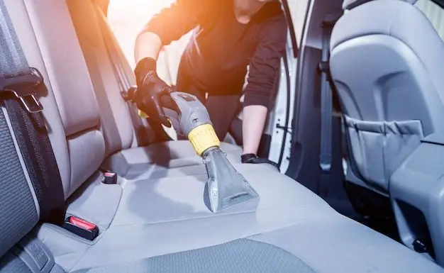 Person cleaning car seats with a vacuum extractor in the backseat area, emphasizing interior car detailing and maintenance.