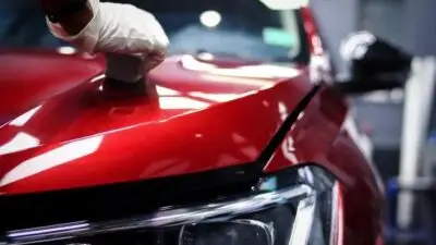 Gloved hand detailing a shiny red car hood in an auto workshop, emphasizing care and maintenance. Perfect for auto detailing content.