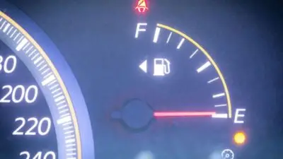 Car fuel gauge showing empty with warning lights on, next to a speedometer.