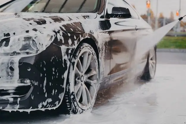 Close-up of a black car being washed with soap and water pressure, highlighting shiny wheels and clean exterior.