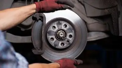 Mechanic wearing gloves inspects and adjusts car brake disc for maintenance in an auto repair shop.