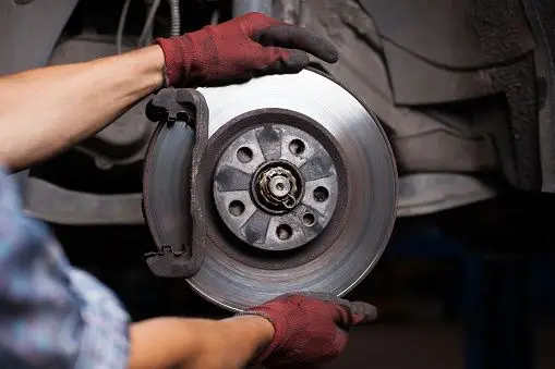 Mechanic wearing gloves inspects and adjusts car brake disc for maintenance in an auto repair shop.