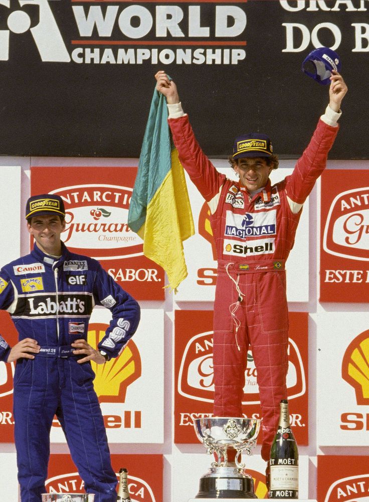 4d8499a3-6649-418c-bff4-ce351b13287f - Engine Stories Two race car drivers celebrating on the podium with trophy at a World Championship event, one holding a flag, smiling.