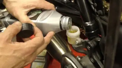 Pouring engine oil into a motorcycle's oil reservoir for maintenance and performance enhancement.