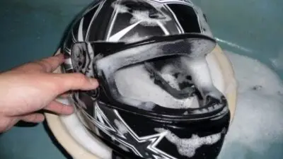 Hand cleaning a motorcycle helmet with soap suds for maintenance and safety.