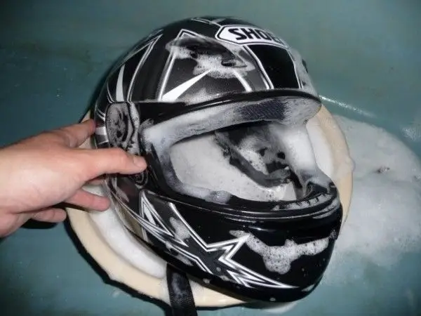 Hand cleaning a motorcycle helmet with soap suds for maintenance and safety.