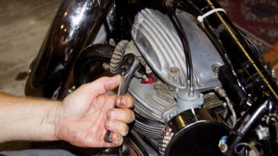Person using wrench to adjust motorcycle engine in garage. Mechanical repair and maintenance concept.