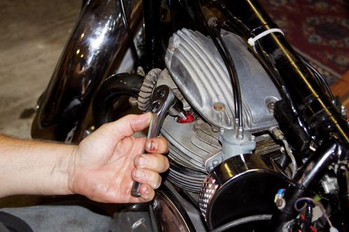 Person using wrench to adjust motorcycle engine in garage. Mechanical repair and maintenance concept.