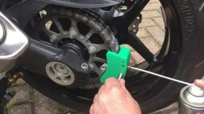 Cleaning a motorcycle chain with a brush tool and lubricant spray for maintenance.