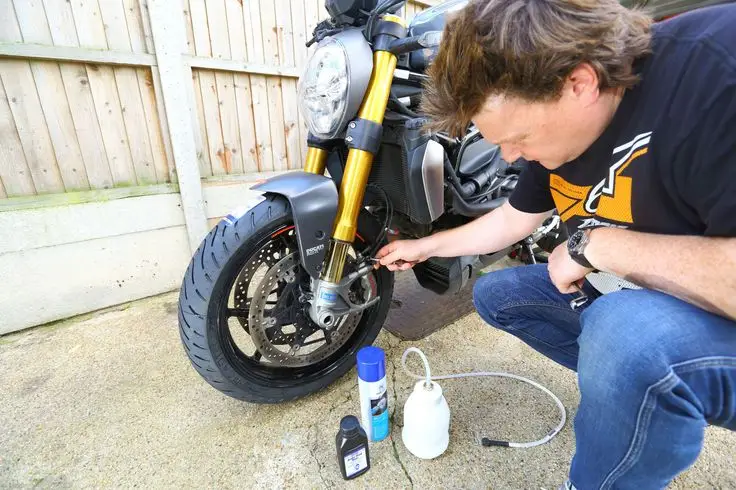 Man servicing motorcycle brakes in driveway, using maintenance tools and products.