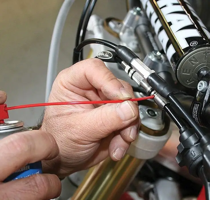 Someone applying lubricant to motorcycle cables for maintenance.