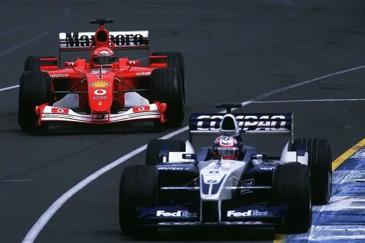 Two Formula 1 cars racing on a track, with a red and a blue car in action, showcasing speed and competitive motorsport action.