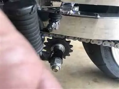 Close-up of a motorcycle chain and sprocket, showcasing mechanical details against a garage floor backdrop.