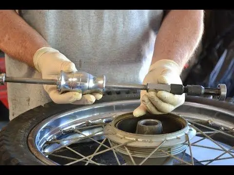 Person using tool to repair a bicycle wheel hub while wearing gloves, focused on maintenance work in a workshop setting.